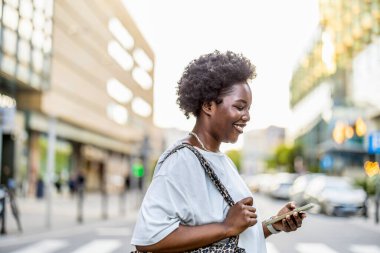 Şehirde cep telefonu kullanan gülümseyen genç bir kadının portresi
