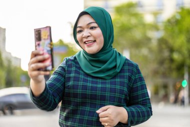 Şehirde cep telefonuyla video görüşmesi yapan Müslüman bir kadın.