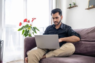 Evdeki kanepede oturan bir adam dizüstü bilgisayar kullanıyor.