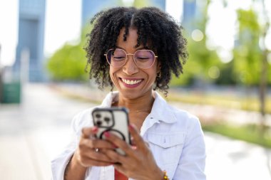Şehirde cep telefonu kullanan gülümseyen genç bir kadının portresi