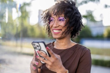 Şehirde cep telefonu kullanan gülümseyen genç bir kadının portresi