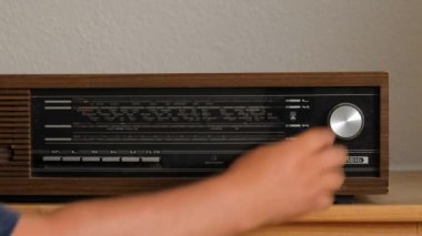Eski ahşap bir homurdanma radyosu. Bir adamın eli radyo dalgasının melodi düğmesini çevirir..
