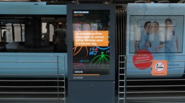 Almanya, Wuppertal, 2022 civarı. Reklam panosuna yakın çekim. Raylı tramvayın arka planında bilgi pankartı.