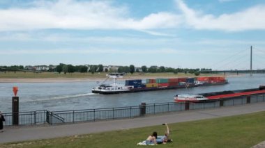 Almanya, DÜZSELDORF, 2022 dolayları. Bir kargo gemisi, konteynırları olan bir mavna rıhtım boyunca Kuzey Ren Nehri boyunca gider. Su altyapısı ile nakliye.