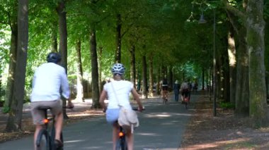 Almanya, Munster, 2022 yılı. Şehir merkezindeki gölgeli ağaçların arasında bir sürü bisikletçi geziniyor..