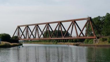 Kırmızı renkli bir yolcu treni Almanya 'da eski paslı bir demiryolu köprüsünden geçen bir su kanalından geçiyor..
