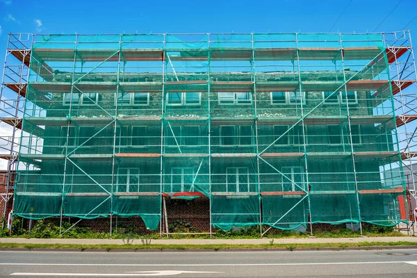 Scaffolding with green safety netting near a multi-story brick house under construction in Germany.