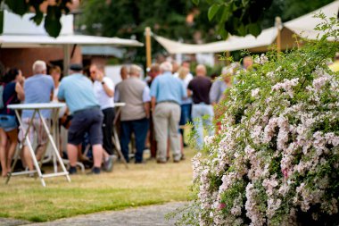 Masanın etrafında duran bir grup insan ve Almanya 'da arka planda şemsiyeler..