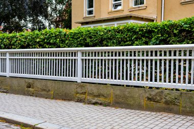 Almanya 'da taş duvarın yanında beyaz çit ve arkasında yeşil çalı vardı..