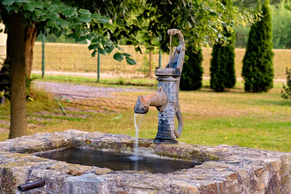 An old cast iron hand pump water column is equipped for a decorative waterfall fountain in the backyard.