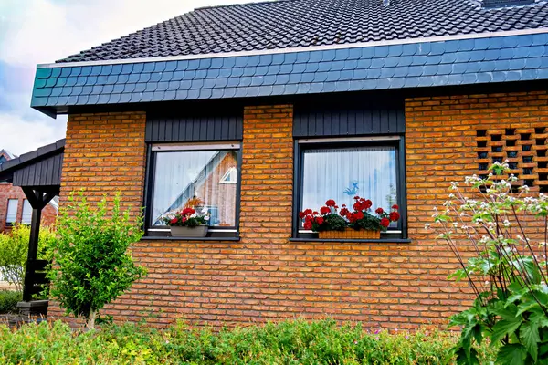 Almanya 'da pencere eşiğinde iki pencere ve çiçekli kırmızı tuğla bina.