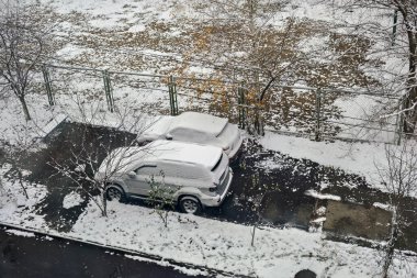 Karla kaplı araba çitin yanındaki karlı sokağa park edilmiş..