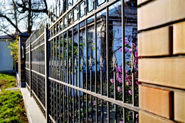 Üzerinde mor çiçekler olan beyaz evin önüne demir çit örmüş..