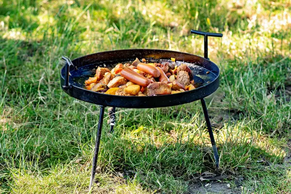 Portable grill is cooking sausages and cut up meat.
