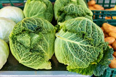 Tahta masanın üzerinde diğer sebzelerin yanında duran yeşil lahana yığını..