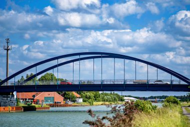 Mavi köprü nehir genişliğinde, içinden arabalar ve kamyonlar geçiyor..