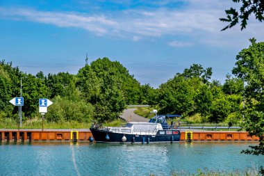 Tekne, insan yapımı sudan yapılmıştır. Etrafı ağaçlar ve karadaki çimlerle çevrilidir..
