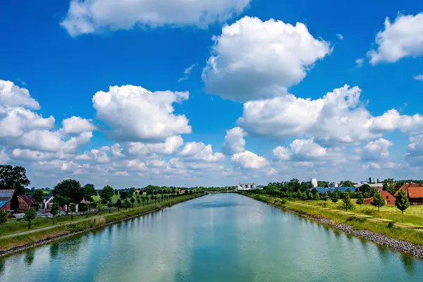 River flows past neighborhood on sunny day with white clouds in the sky.