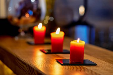 Ahşap bir masada, siyah bardak altlığı üzerinde üç mum.