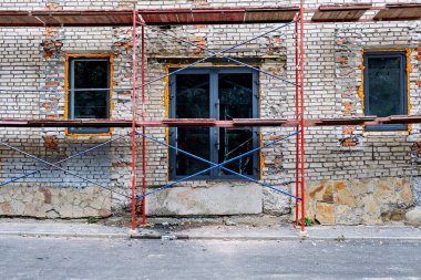 İnşaat halindeki tuğla duvarları ve mavi çerçeveli geniş pencereli bir bina.