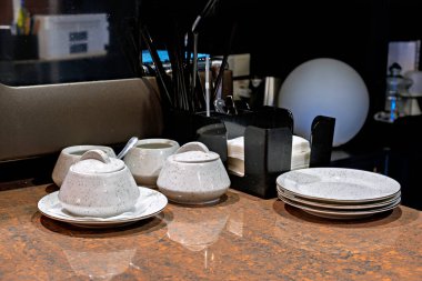 Kahverengi mermer bir tezgahta beyaz seramik bardaklar ve çay tabakları koleksiyonu.
