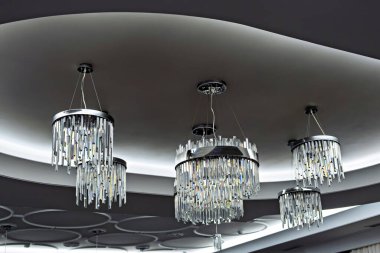 Birden fazla kolu olan modern bir avize. Her biri tavandan sarkan bir kristal kümesini kavisli bir tasarımla tutuyor.