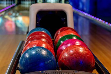 Bu resim, topun geri dönüşünde dizilmiş renkli bowling toplarının olduğu bir bowling salonunu gösteriyor.