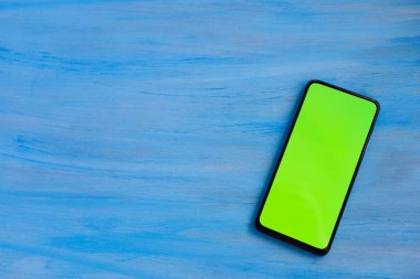 Phone smartphone, green screen on Blue wood background top view.
