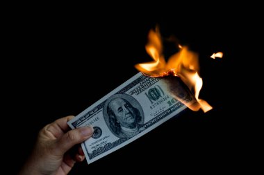 Banknot tutan bir el yanıyor, nakit para iş ödemesini ve finansal başarıyı simgeliyor