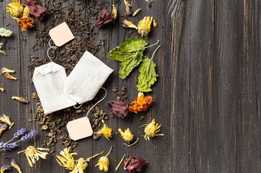 Composition of dry black and green tea, tea bags and dry hibiscus, calendula, lavender flowers on a dark wooden background top view close-up copy space. Different types of dry tea on a dark background with place for text.