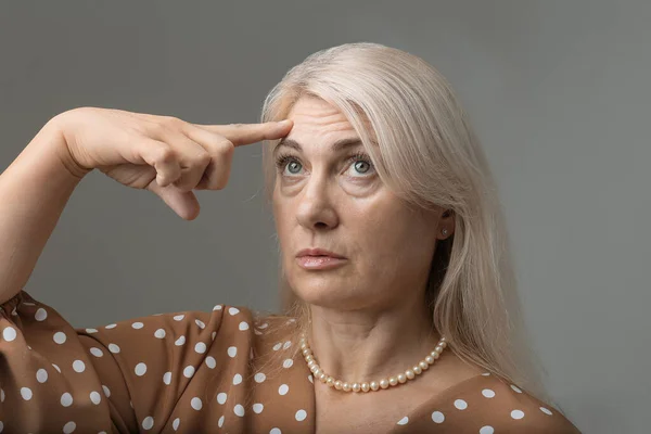 A woman points her finger at the wrinkles on her forehead. Portrait of an adult woman with wrinkles on her face. Anti-aging treatments, botox, fillers, mesotherapy, mesothreads.
