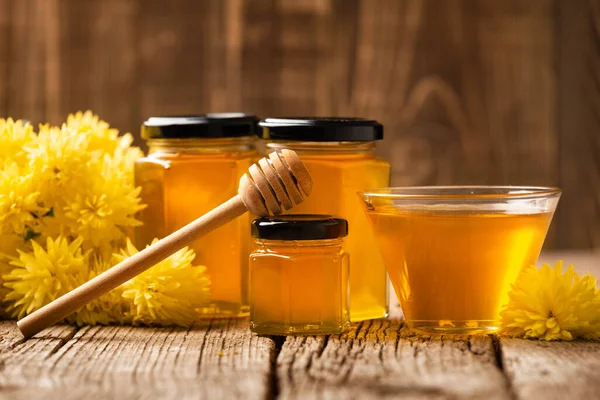 在玻璃瓶和玻璃碗中 木制传送器和木制背景下的花朵中 蜂蜜的创意组合特写 有机蜜蜂产品的概念 — 图库照片