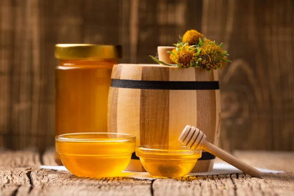 有机蜜蜂产品的概念组成 罐中的蜂蜜 透明的碗和带有蜂蜜的木制桶在天然木制背景上 — 图库照片