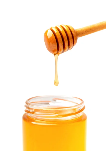 有機蜂蜜は 白い背景のガラスの透明な瓶のクローズアップにディッパーから注ぎ込まれます 蜂蜜の棒から瓶に流れ込みます 分離の皿から蜂蜜を注ぐ — ストック写真