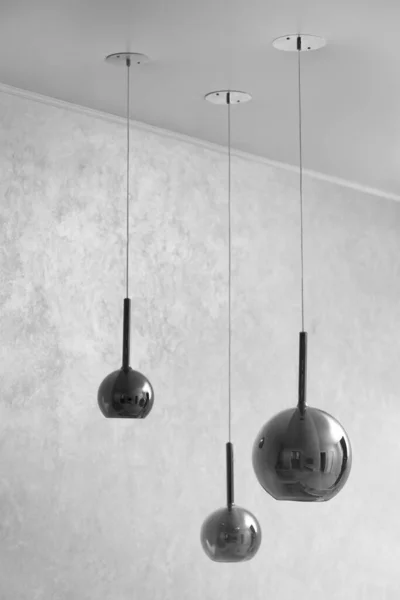 stock image Three contemporary chandeliers in glossy gray glass against a textured gray wall with space for text. Chandeliers in the form of balls of different sizes hang on the ceiling at different heights.