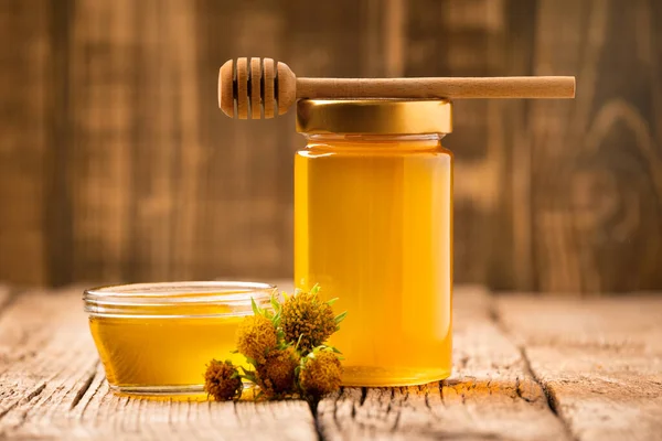 在一个玻璃瓶和一个碗 一个木制的斗篷和黄色的花在一个老化的木制背景创造性的蜂蜜组合 有机蜜蜂产品的概念 — 图库照片