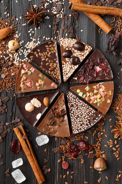 Creative composition chocolate pizza and ingredients on a dark background top view, pizza shaped chocolate with candied fruits, nuts, dry berries, chocolate on a wooden background.