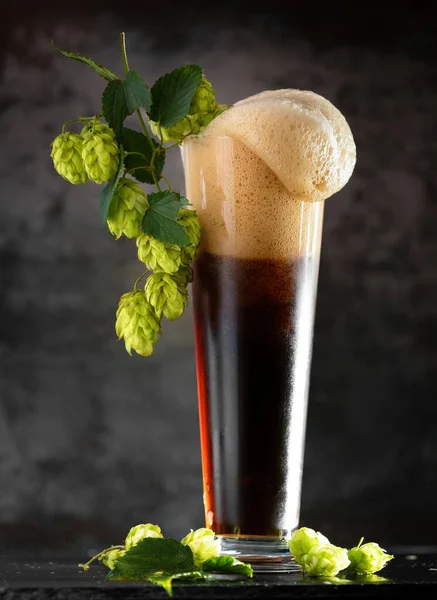 杯子里的黑啤酒 褐色背景的木制桌子上的绿色跳跃 天然啤酒的概念 酿造传统Oktoberfest 啤酒节 圣帕特里克节 — 图库照片