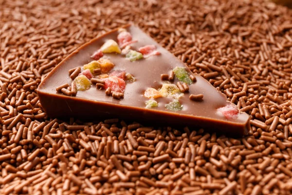 Chocolate background. A piece of chocolate pizza with candied fruits lies in chocolate chips close-up. The concept of confectionery.