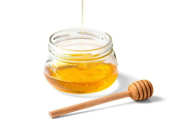 白い背景のクローズアップに 空のガラスの透明な瓶と木製の皿に蜂蜜が注がれます 有機蜂蜜は隔離されたボウルに流れ込む 蜂蜜マクロ写真を入れる — ストック写真