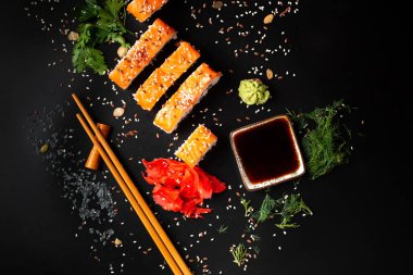 Set of salmon rolls on a dark background with chopsticks, sauce and red ginger. Red sushi with sesame on black background