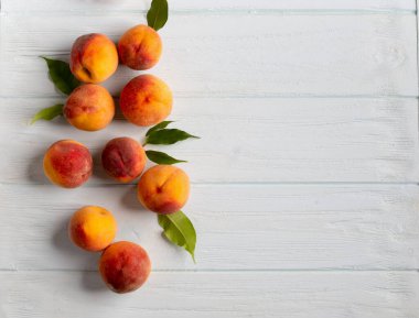 Yeşil yapraklı şeftaliler beyaz ahşap arka planda yatar. Olgun şeftaliler eski ahşap arka plan görünümüne yakın