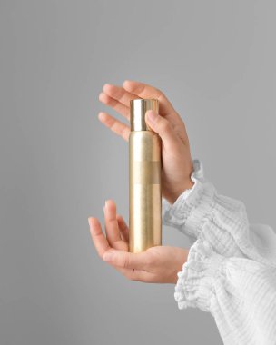 Kız, elleri gri bir arka planda bir şişe saç spreyi tutuyor. Kadınların elleri nazikçe bir sprey şişesini tutar..