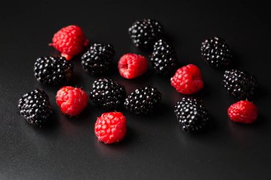 A handful of raspberries and blackberries on a black background close-up. Healthy fruits on a dark background with water drops