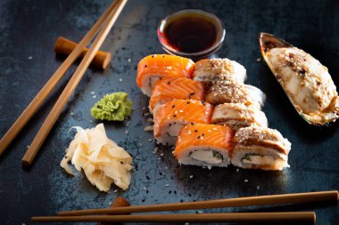 Set of salmon rolls on a dark background with chopsticks, sauce and red ginger. Red sushi with sesame on black background