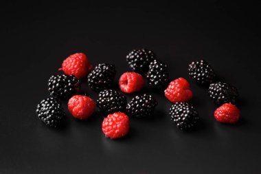 A handful of raspberries and blackberries on a black background close-up. Healthy fruits on a dark background with water drops