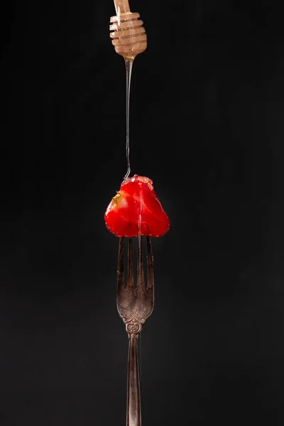 Half of a strawberry on an old fork on a dark background close-up. Honey flows over strawberries.