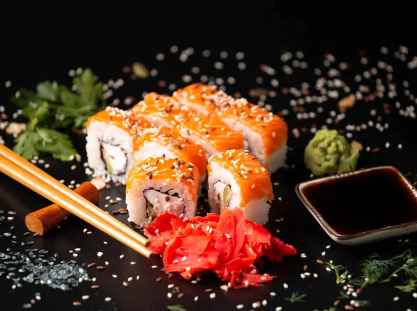 Set of salmon rolls on a dark background with chopsticks, sauce and red ginger. Red sushi with sesame on black background