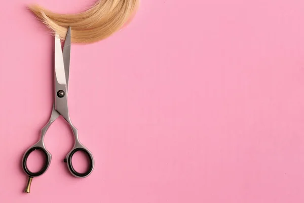 Scissors and piece of blond hair. Professional barber hair cutting shears on background. Hairdresser salon equipment concept, premium hairdressing set. Accessories for haircut with copy space