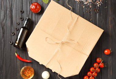 Kapalı bir kutuda pizza, soslar, baharatlı zeytin yağı, koyu ahşap arka plan manzaralı taze sebzeler. Yemek teslimatı.